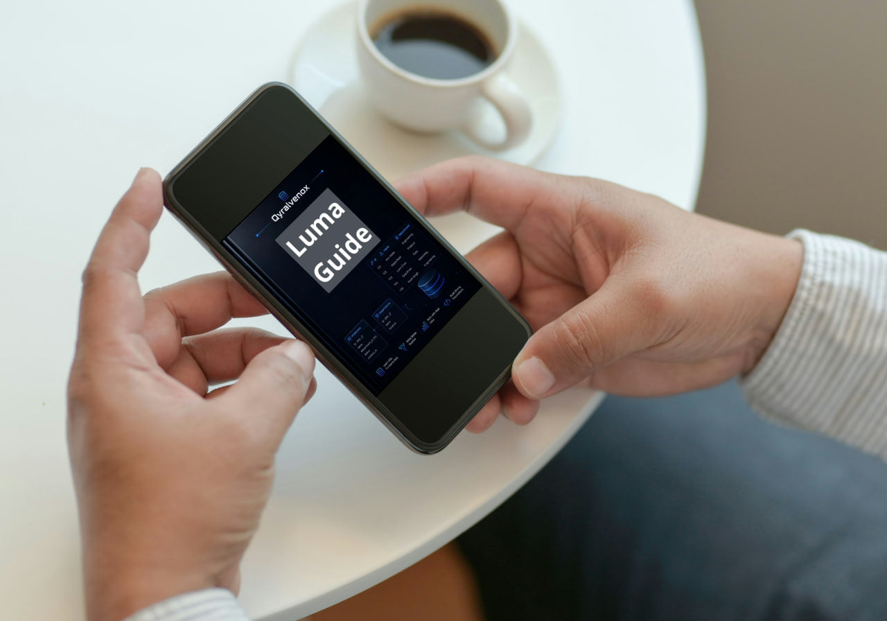 A person holds a black smartphone displaying the 'Luma Guide' app over a white table next to a cup of coffee.